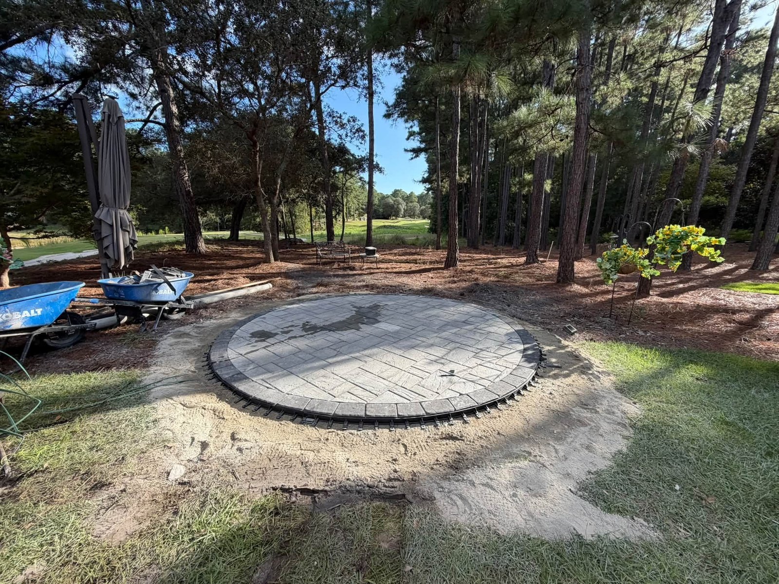 Twelve foot diameter circular paver fire pit patio installed among pine trees overlooking a golf course in Ocean Ridge Plantation