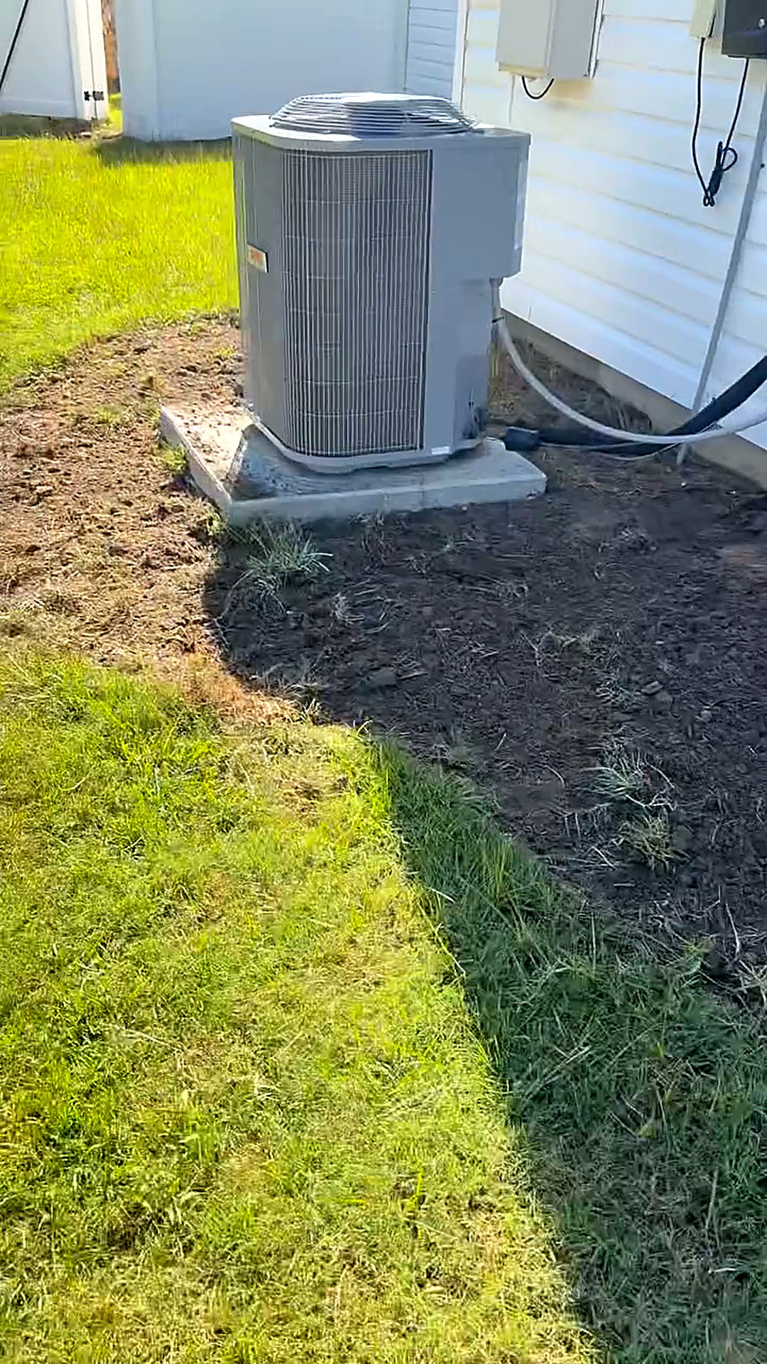 Bare damaged lawn around an outdoor air conditioning unit beside a house before new sod was installed