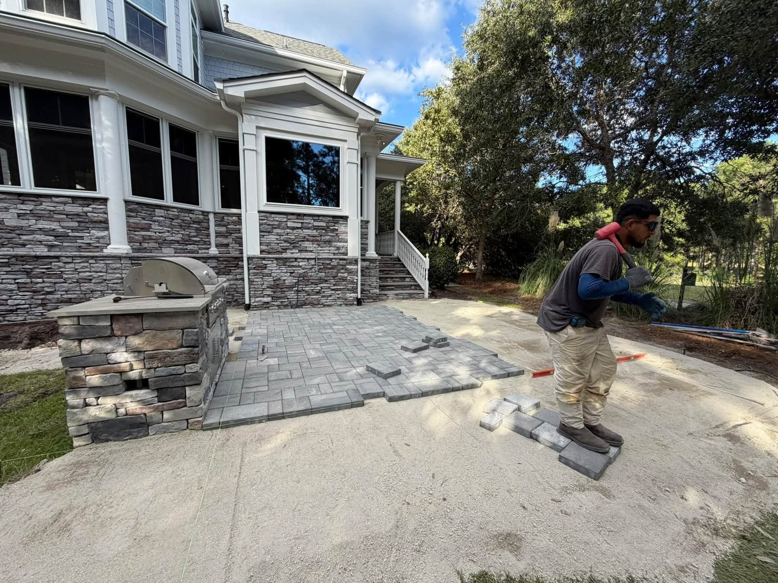 Hardscape installer carrying a rubber mallet across a partially completed paver patio in coastal Brunswick County North Carolina