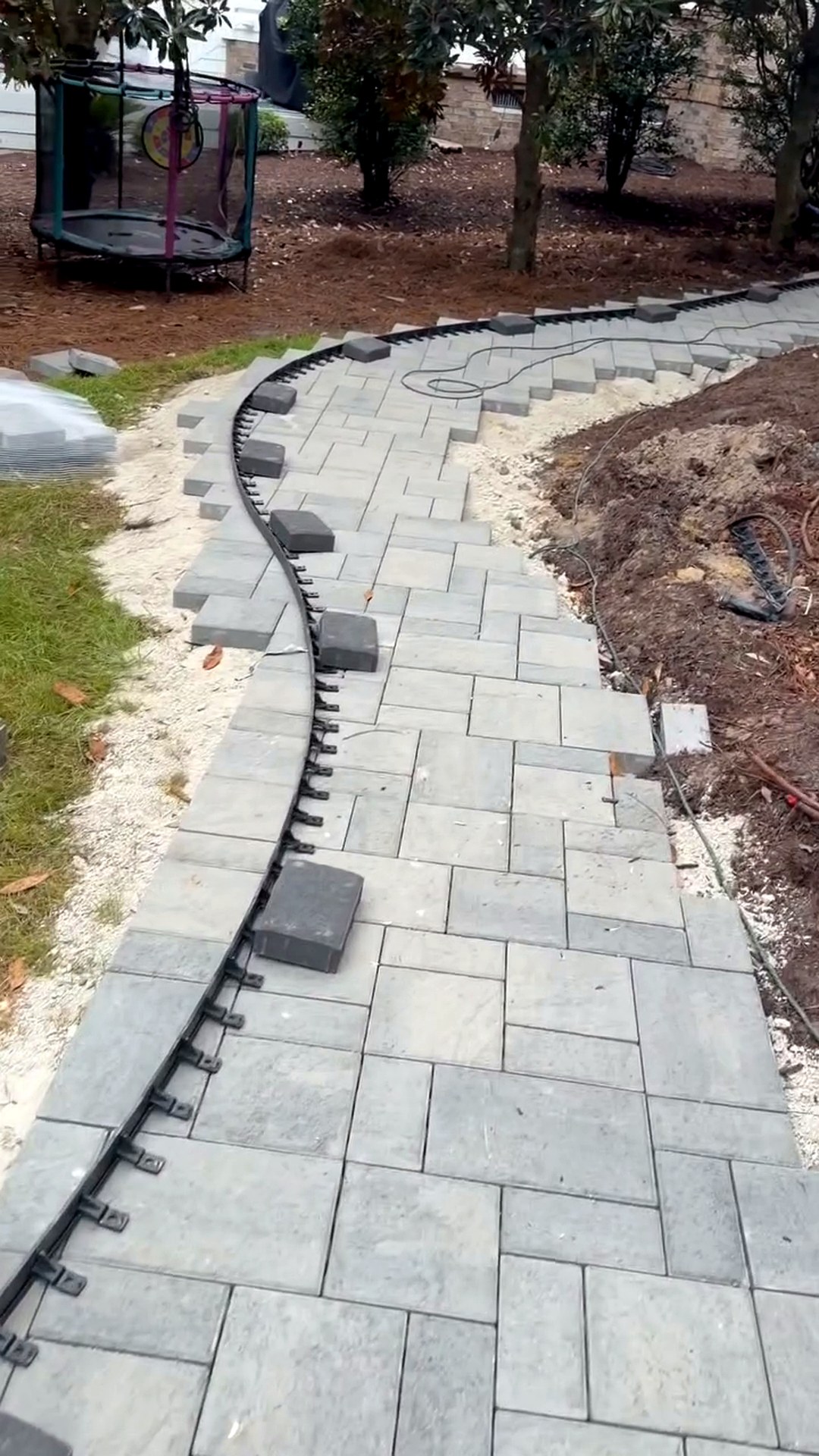 Black edge restraint following the marked S-curve of a paver walkway under construction in Ocean Ridge Plantation, Ocean Isle Beach NC
